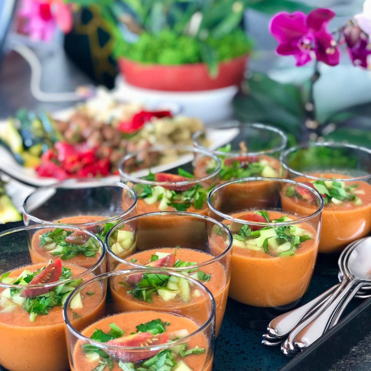 Cups of gazpacho topped with diced veggies on a tray.