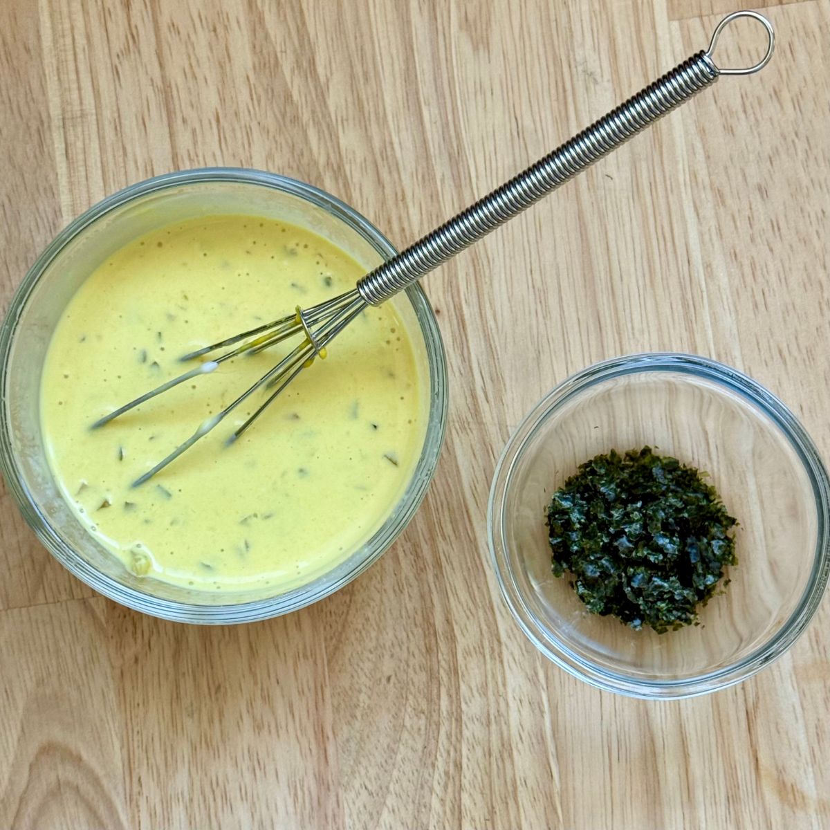 A bowl filled with dressing for vegan tuna salad and a bowl of ground nori flakes.