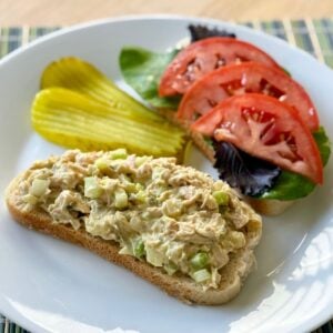 A plate with an open-face vegan tuna salad sandwich and pickle slices.