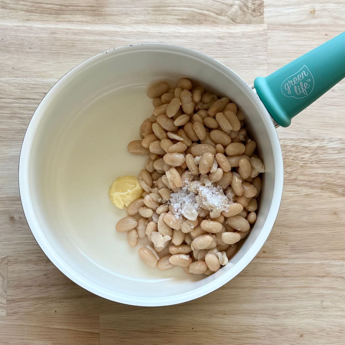 A sauce pan with white beans and vegan butter.