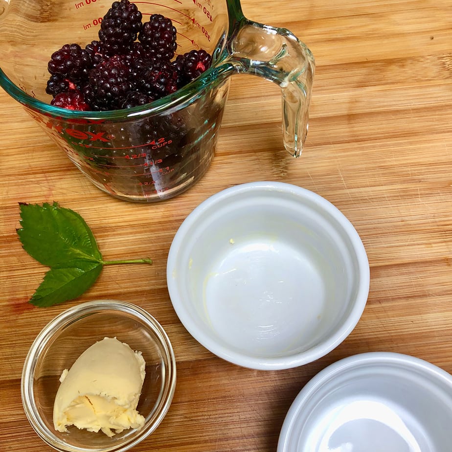 A measuring cup with fresh boysenberries and small ramekins with butter.