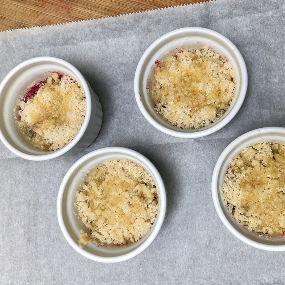Butter drizzled on top of individual baking dishes with boysenberry crumble.
