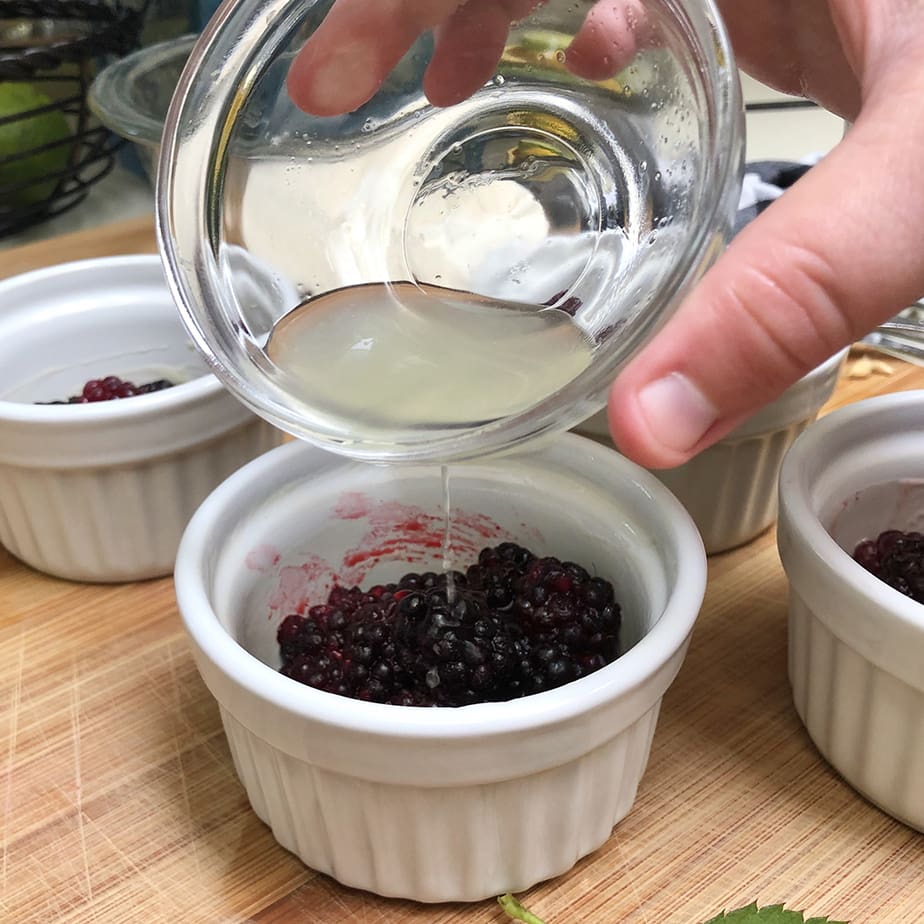 Lemon juice poured over boysenberries in ramekins.