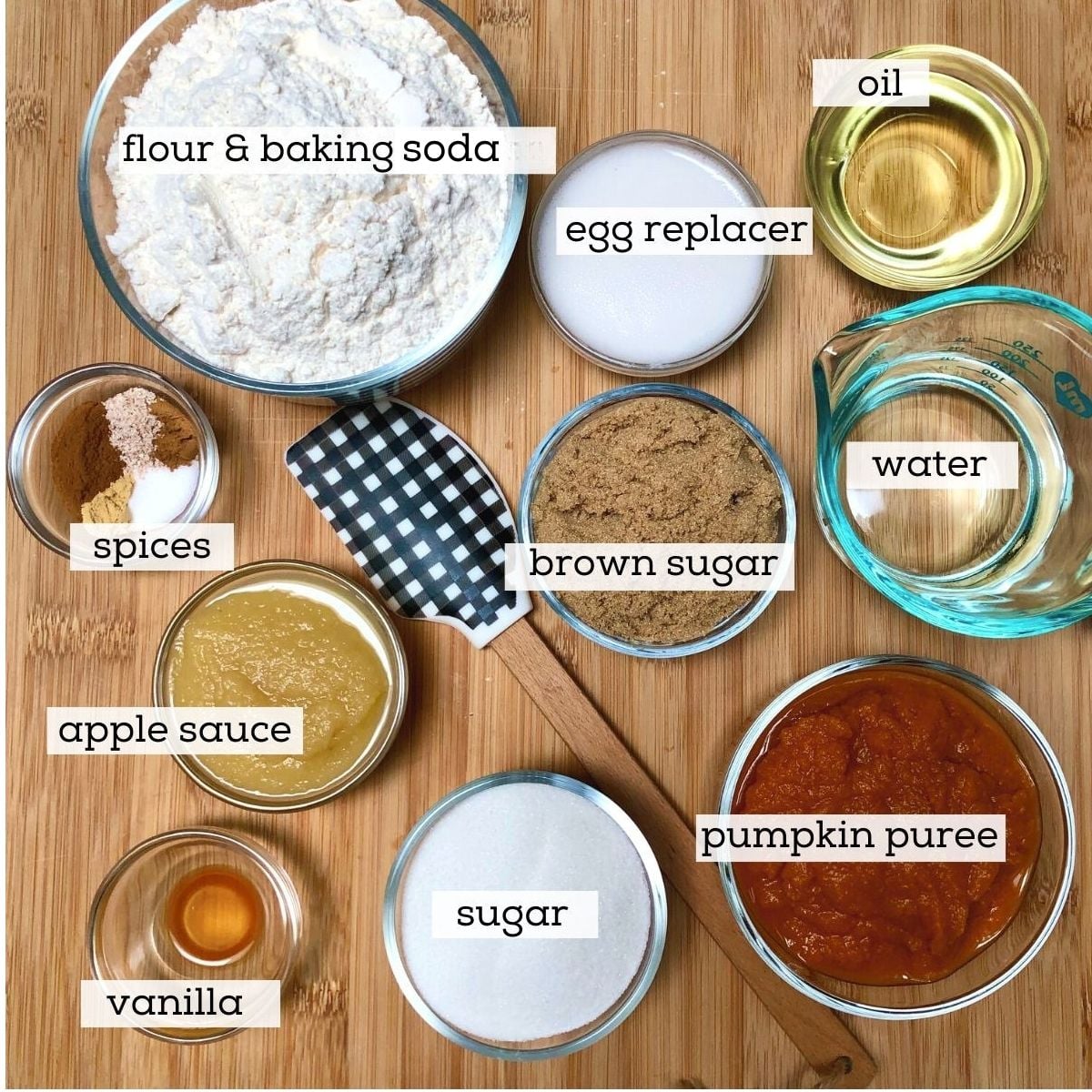 Ingredients for making vegan pumpkin bread, including: flour, baking soda, egg replacer, oil, spices, brown and white sugar, applesauce, vanilla, water, and pumpkin puree.
