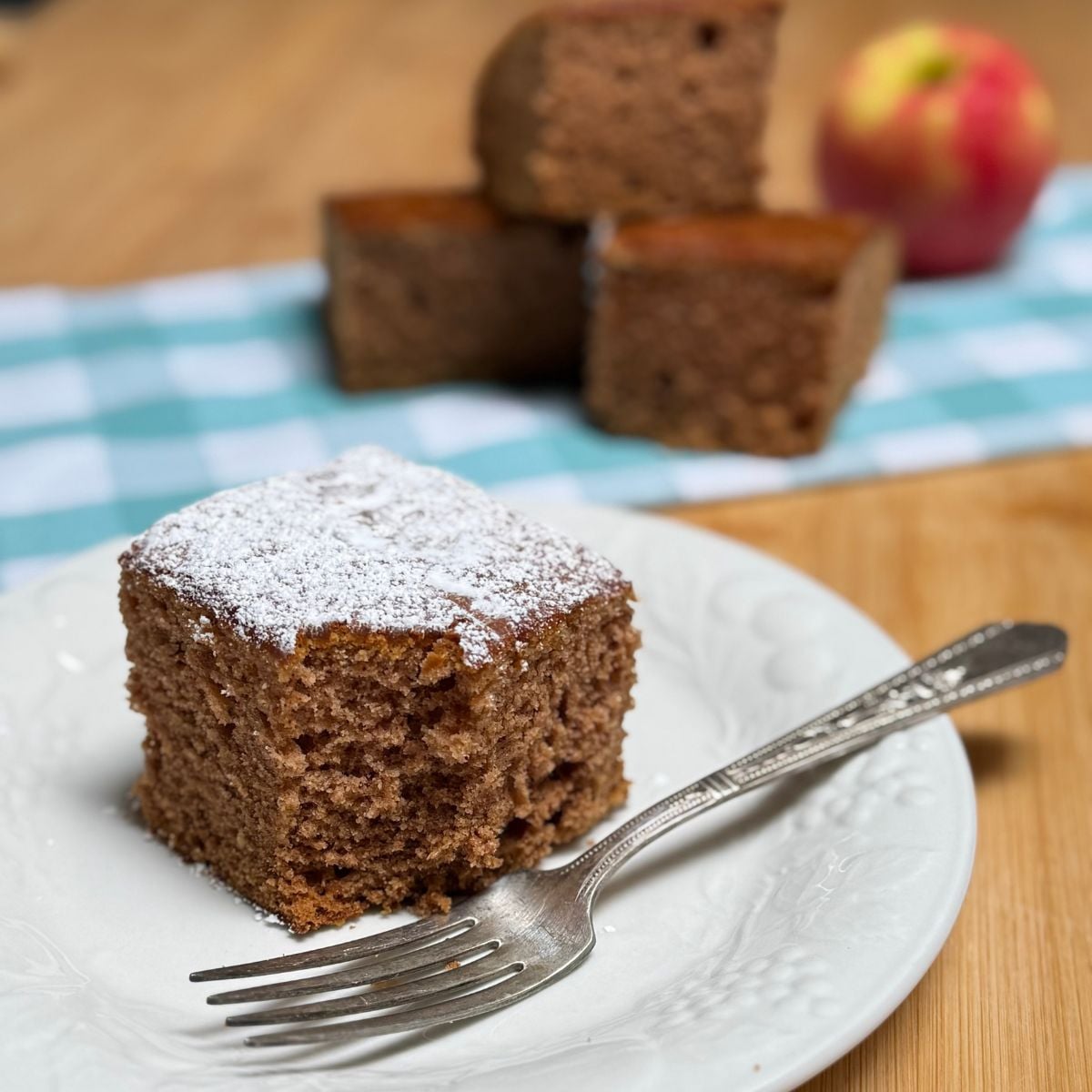 A slice of vegan applesauce cake topped with powdered sugar on a plate.