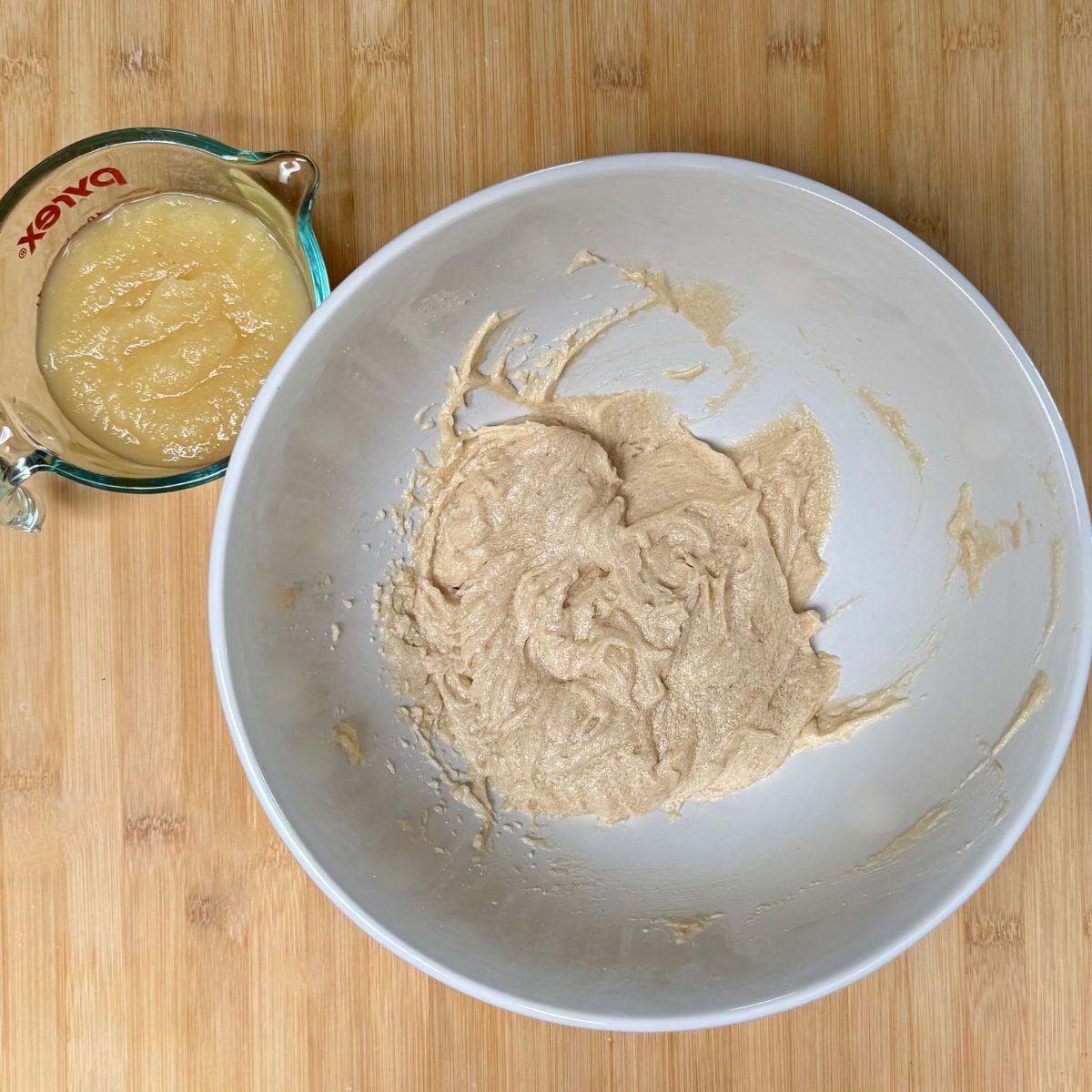 A mixing bowl filled with batter and a measuring cup with applesauce for making a cake.
