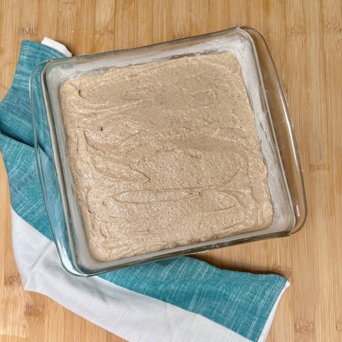 A square baking dish filled with vegan applesauce cake batter.