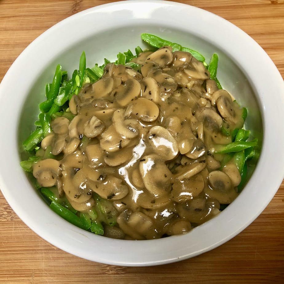 A casserole dish with uncooked green beans topped with mushroom gravy.