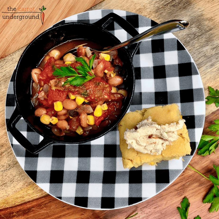 a bowl of vegan chili with a slice of homemade vegan cornbread on a checkered plate