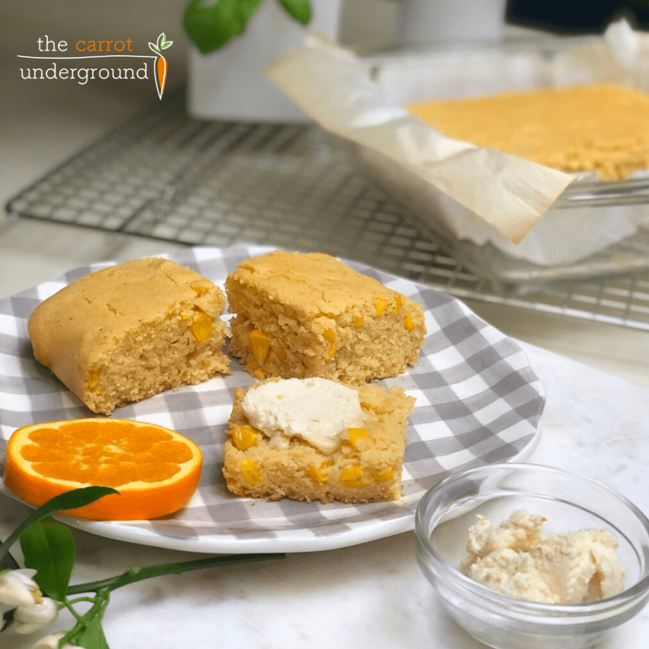 slices of homemade vegan cornbread on a checkered plate with orange slices and butter