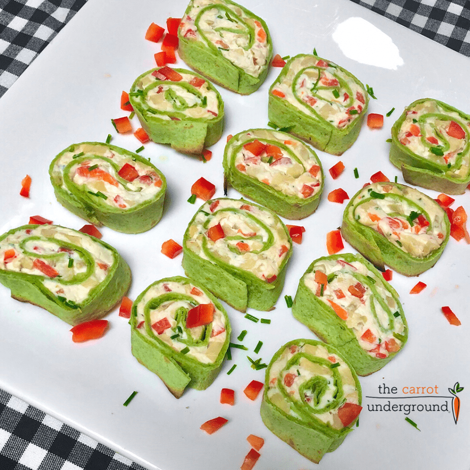 a platter of vegan fiesta pinwheels made with spinach tortillas filled with vegan cream cheese, olives, artichoke hearts & red bell pepper