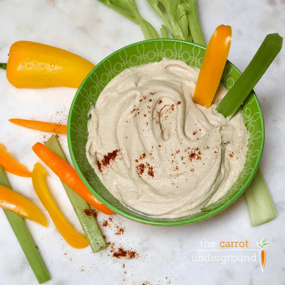 a bowl of creamy homemade hummus with pepper slices and celery