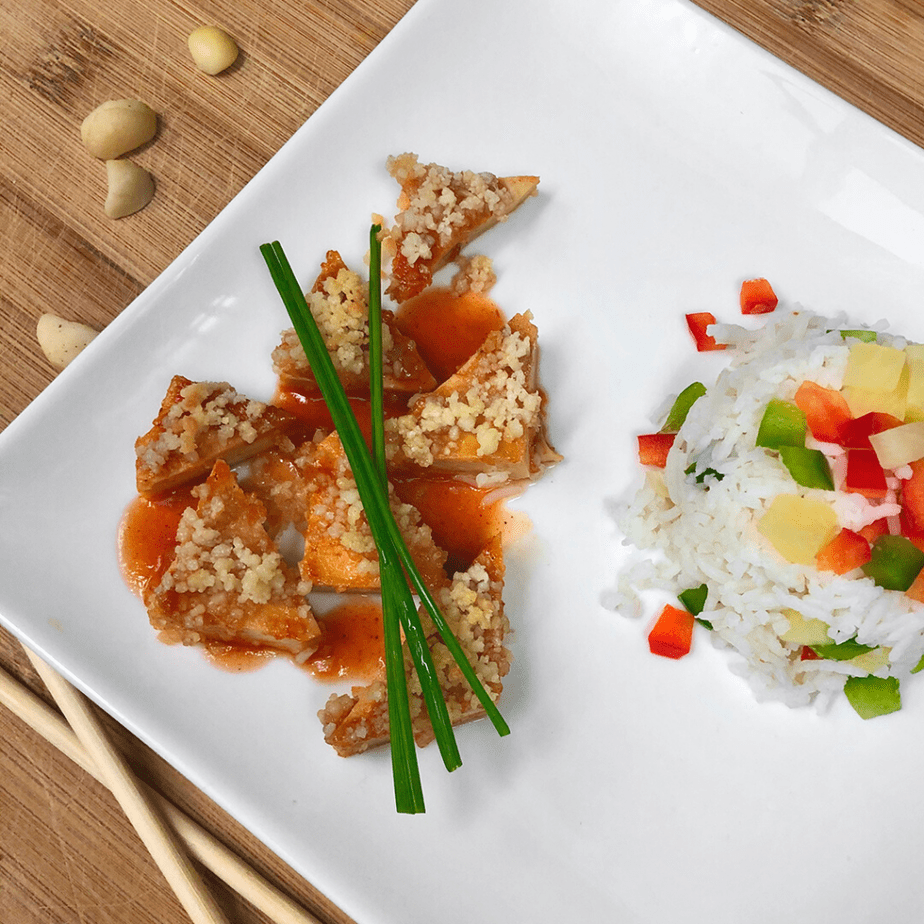 Triangles of vegan sweet & sour tofu and rice with chives on a plate.