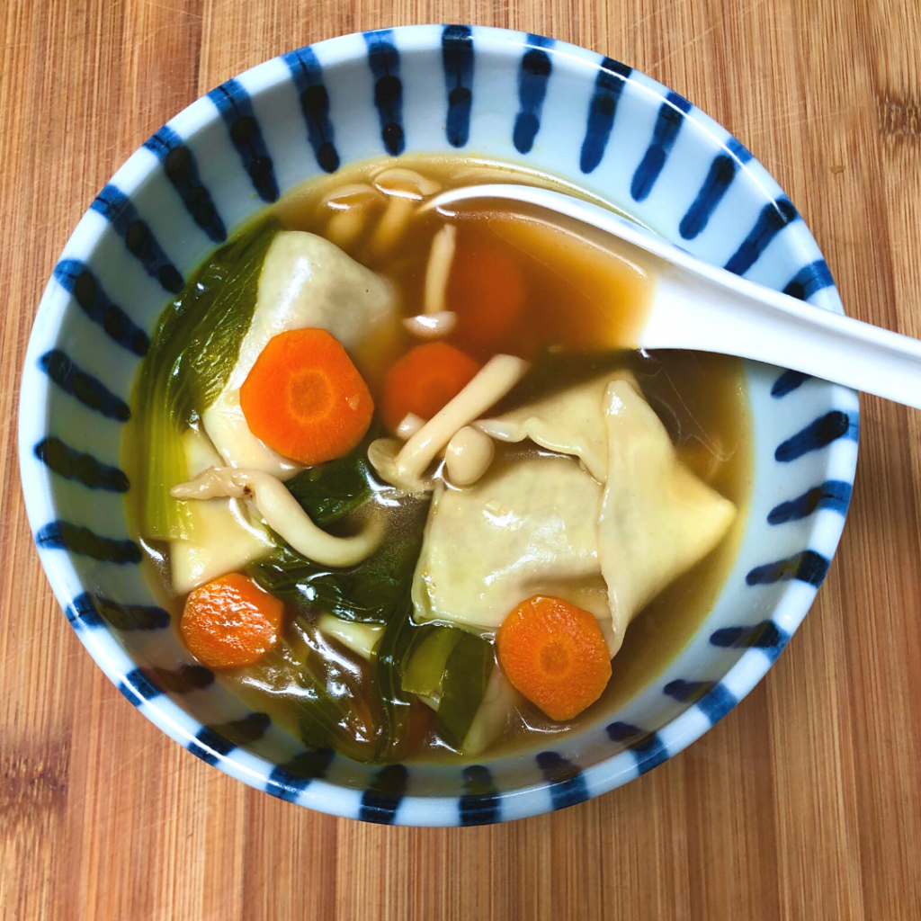A bowl of vegan wonton soup with carrots and bokchoy.