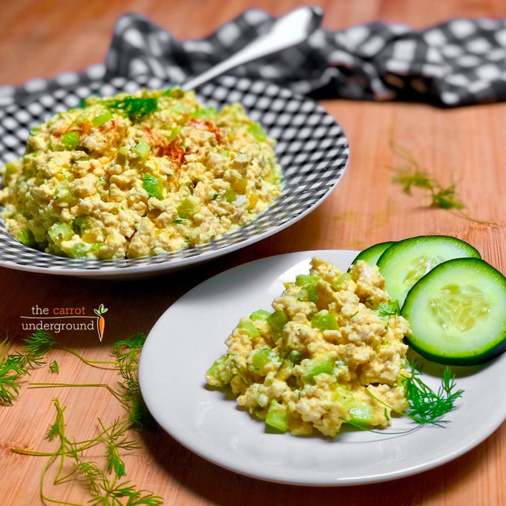 Two dishes filled with vegan eggless salad and cucumber slices.
