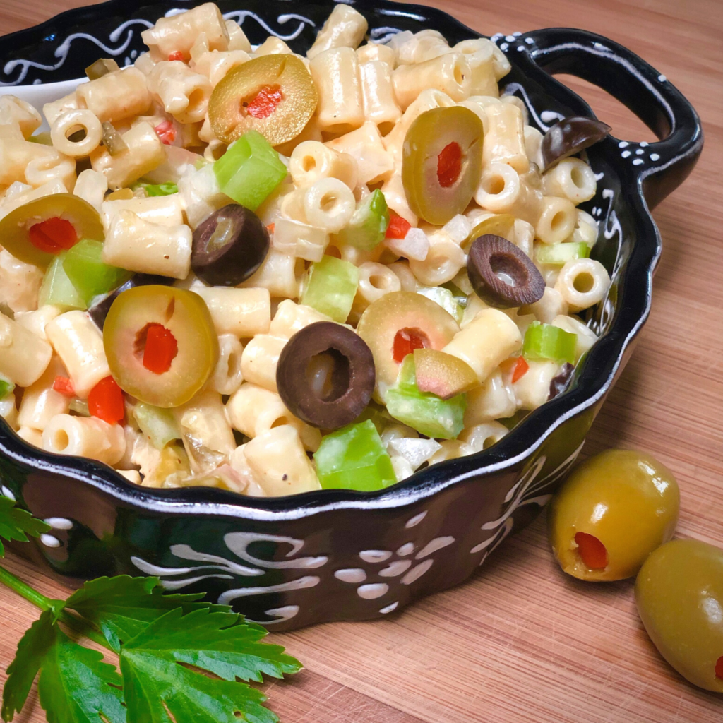 A black and white dish with vegan macaroni salad made with black and green olives, celery, onion and vegan mayo dressing.
