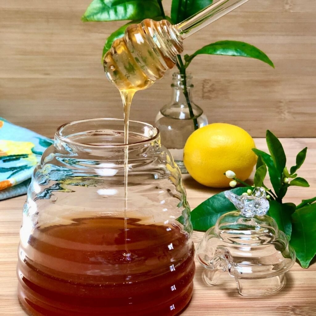 Vegan honey made with apple juice and clover, drizzling from a honey dipper into a jar.