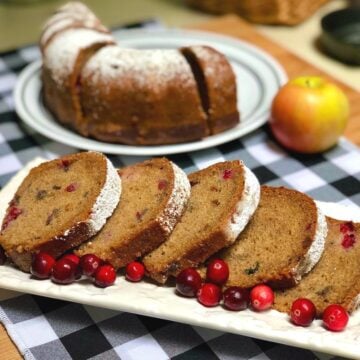 Slices of vegan applesauce cake arranged on a plate with fresh cranberries.
