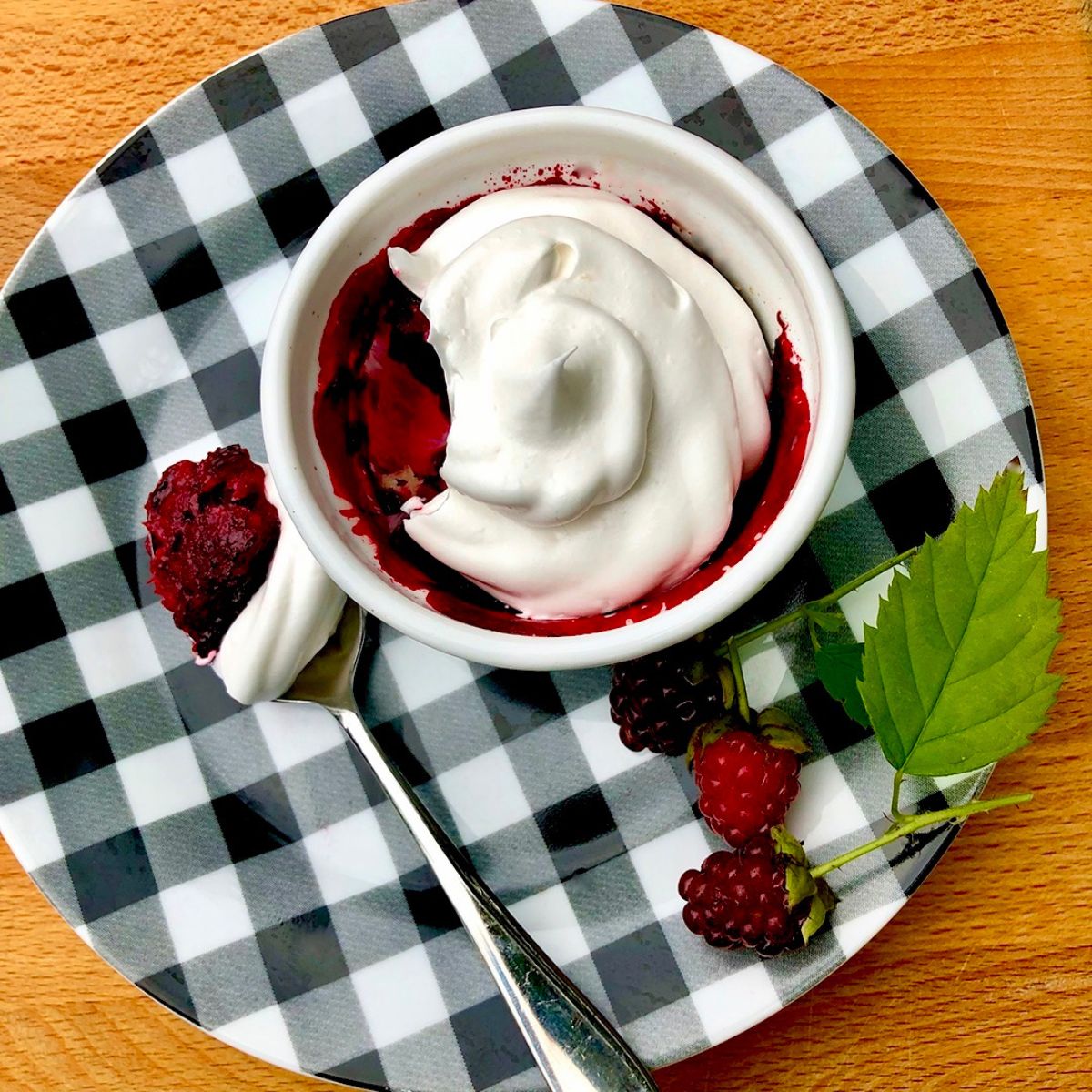 A vegan berry crumble topped with coconut whipped cream on a gingham print plate.