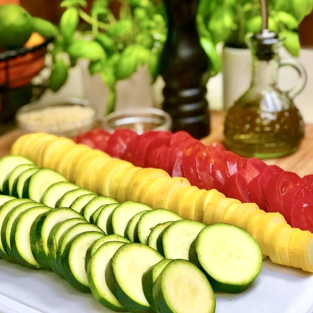 Sliced zucchini, yellow squash, and tomatoes on a cutting board.
