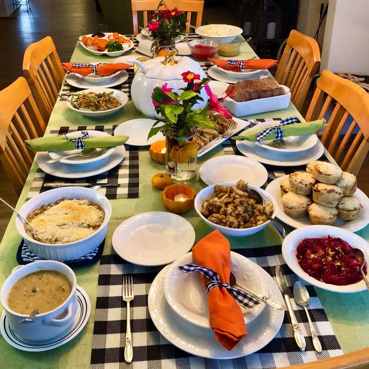 A vegan Thanksgiving dinner table arranged with plant-based dishes including seitan Wellington, mini tofu and veggie pot pies, balsamic Brussels sprouts, mashed potatoes, dressing, cranberries, candied yams.