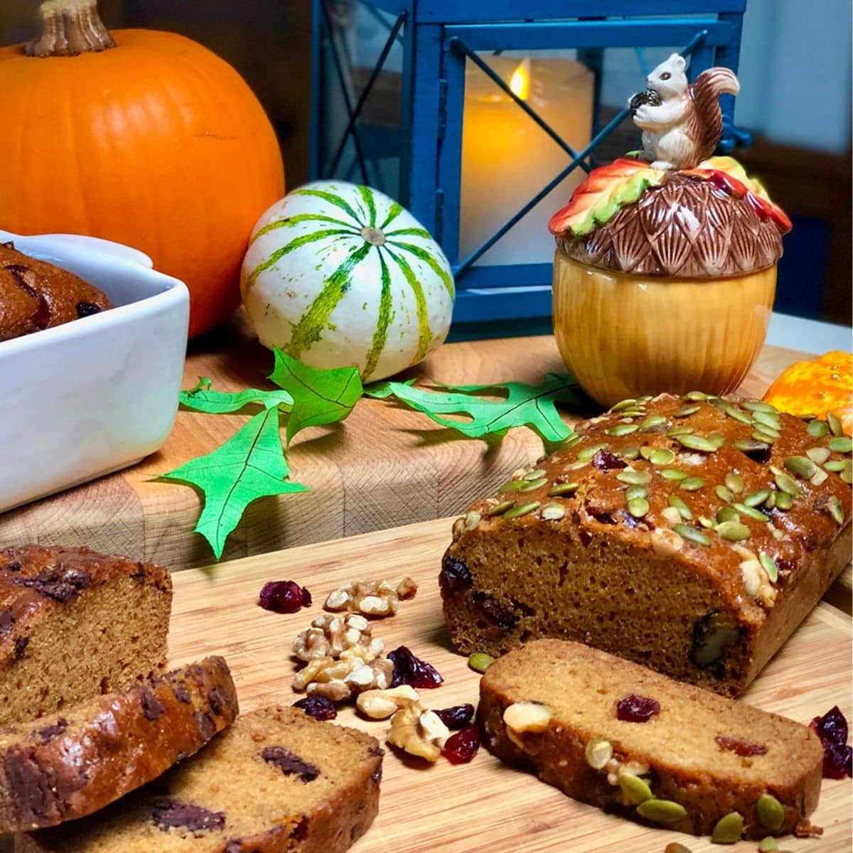 Loaves of vegan pumpkin bread, pumpkins, a decorative dish, and a lantern.