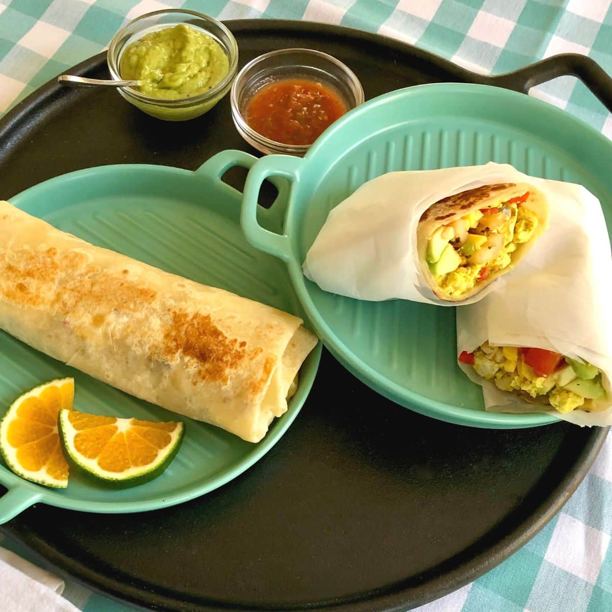 Plated vegan California breakfast burritos made with tofu scramble, hash brown potatoes, plant-based cheese, avocado, tomatoes, and salsa wrapped in a flour tortilla.