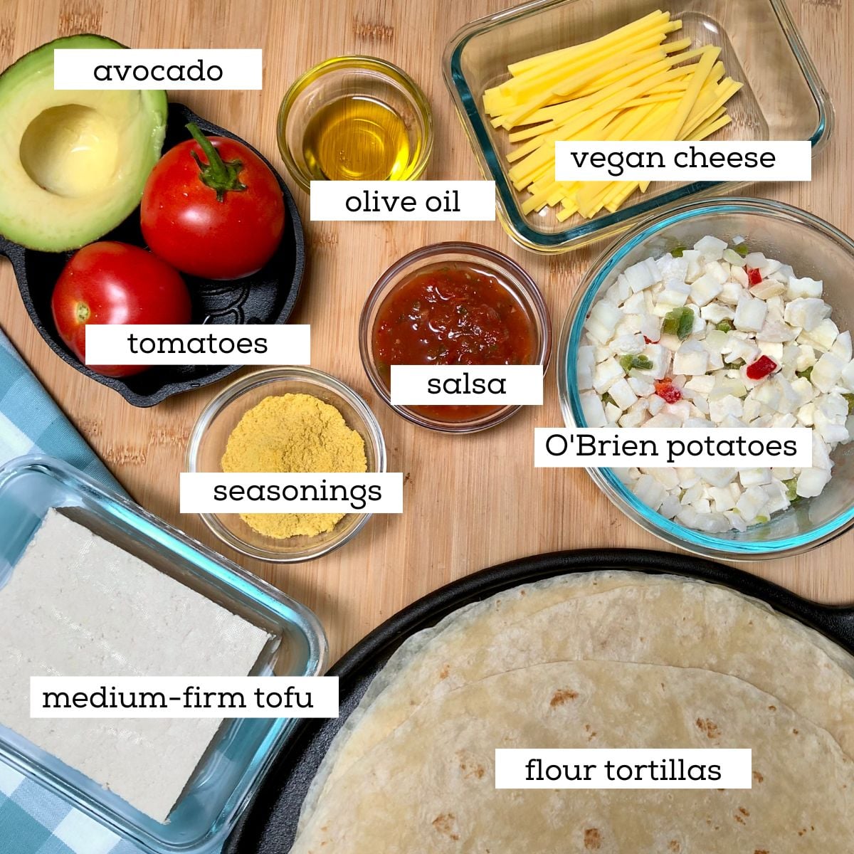 Ingredients for making vegan California breakfast burritos, including tofu, O'Brien potatoes, vegan cheese, avocado, tomatoes, salsa, seasonings, and flour tortillas.