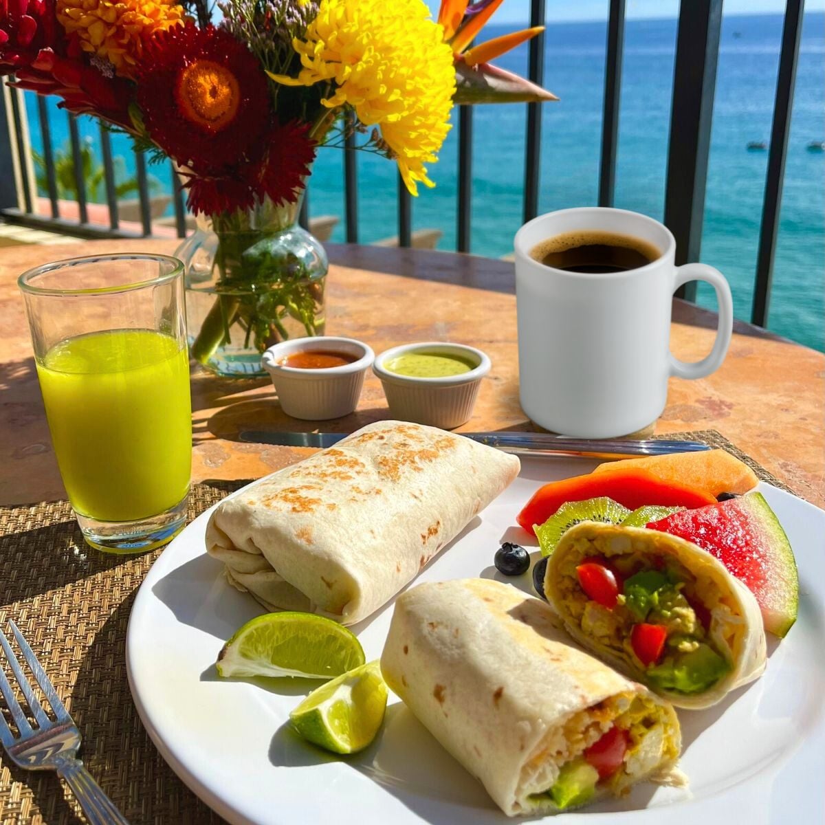 A vegan California breakfast burrito plated with fruit on a table overlooking the ocean.