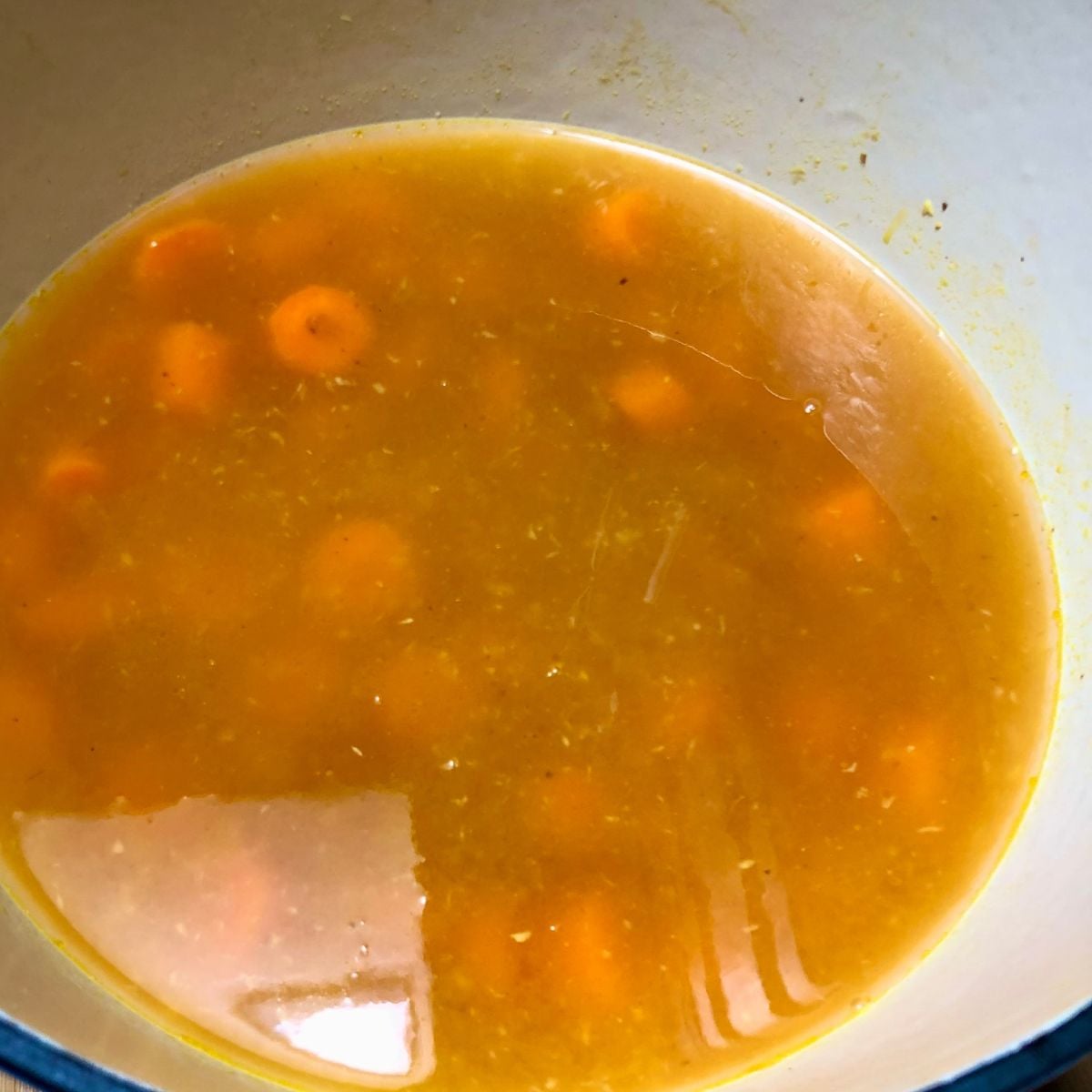 Carrots, ginger, onions, and broth inside a soup pot.