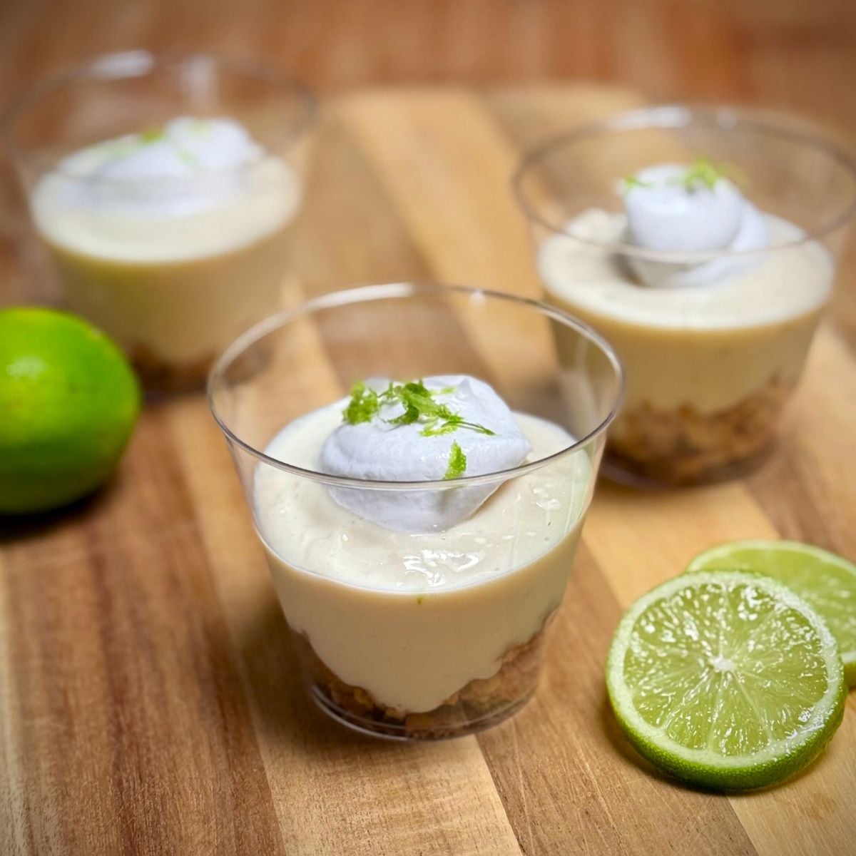 Cups filled with vegan key lime parfaits made with a cookie crumble base layered with creamy key line filling, topped with dairy-free whipped cream and lime zest.