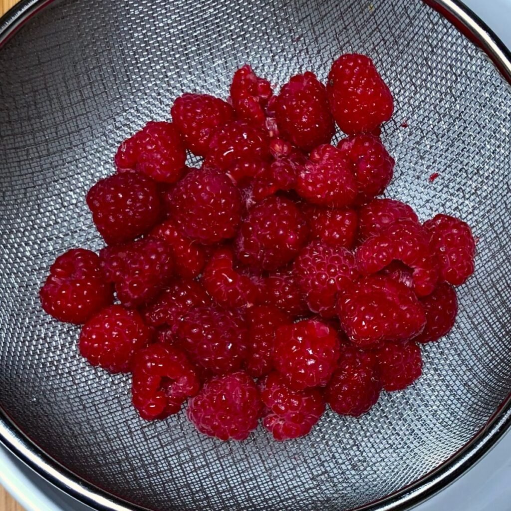 Freshly rinsed raspberries in a strainer.