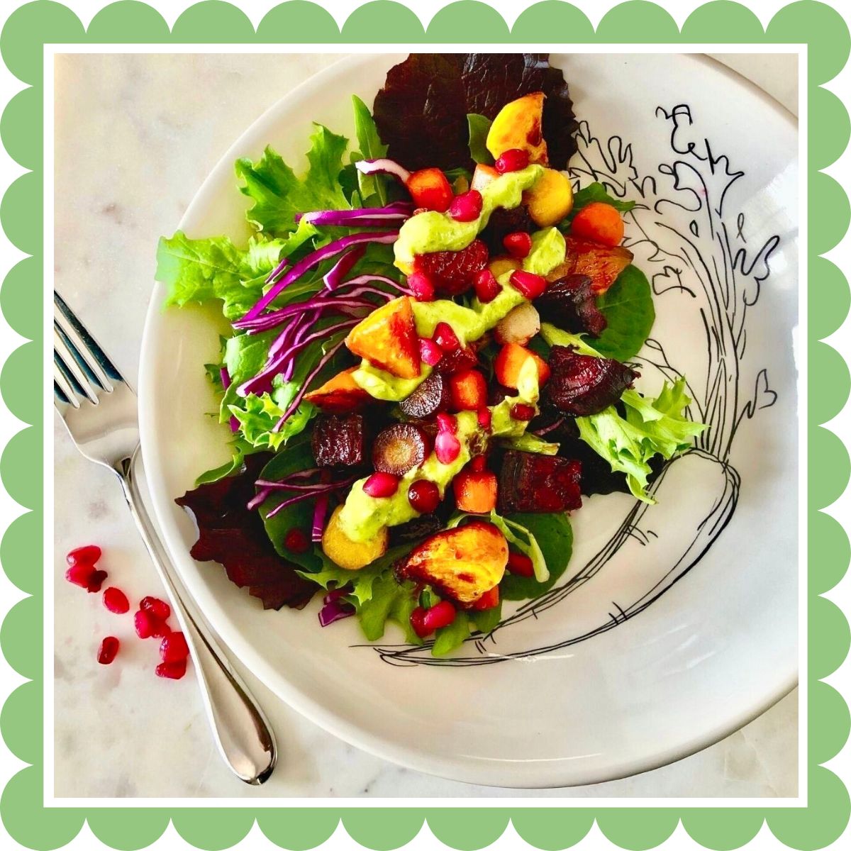 A bowl with roasted root vegetables on a bed of salad greens, topped with avocado basil dressing and pomegranate seeds.