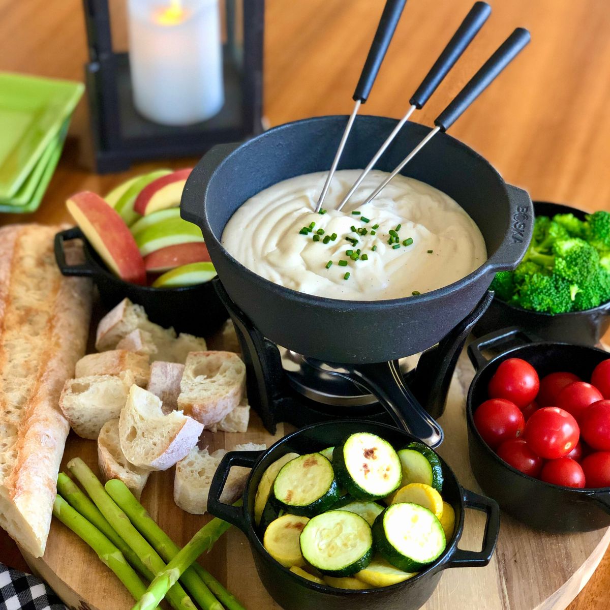 A cast iron fondue pot with vegan cheese fondue surrounded by an assortment of vegetables ans bread for dipping.