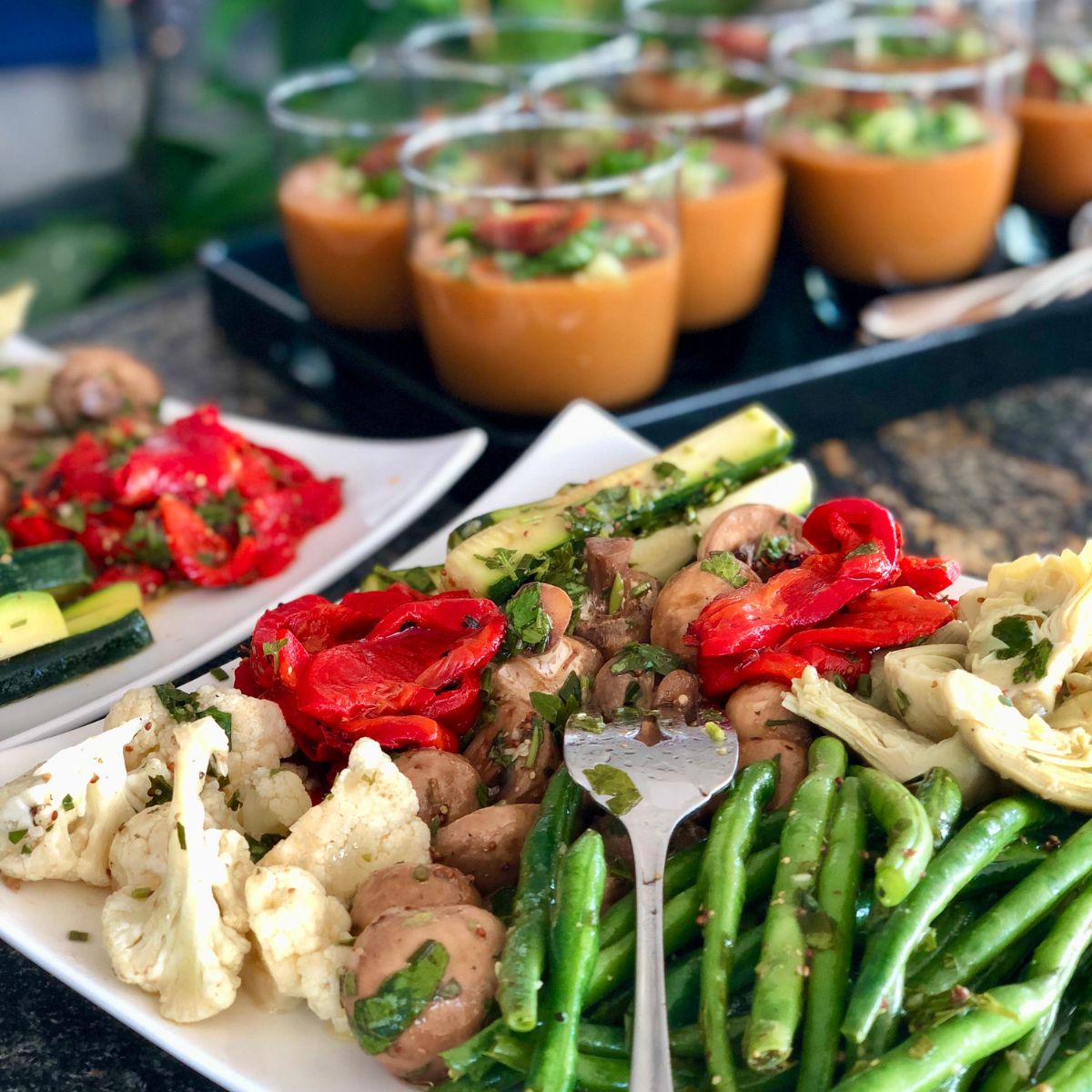 Buffet plates arranged with Mediterranean vegetables and cups of gazpacho.