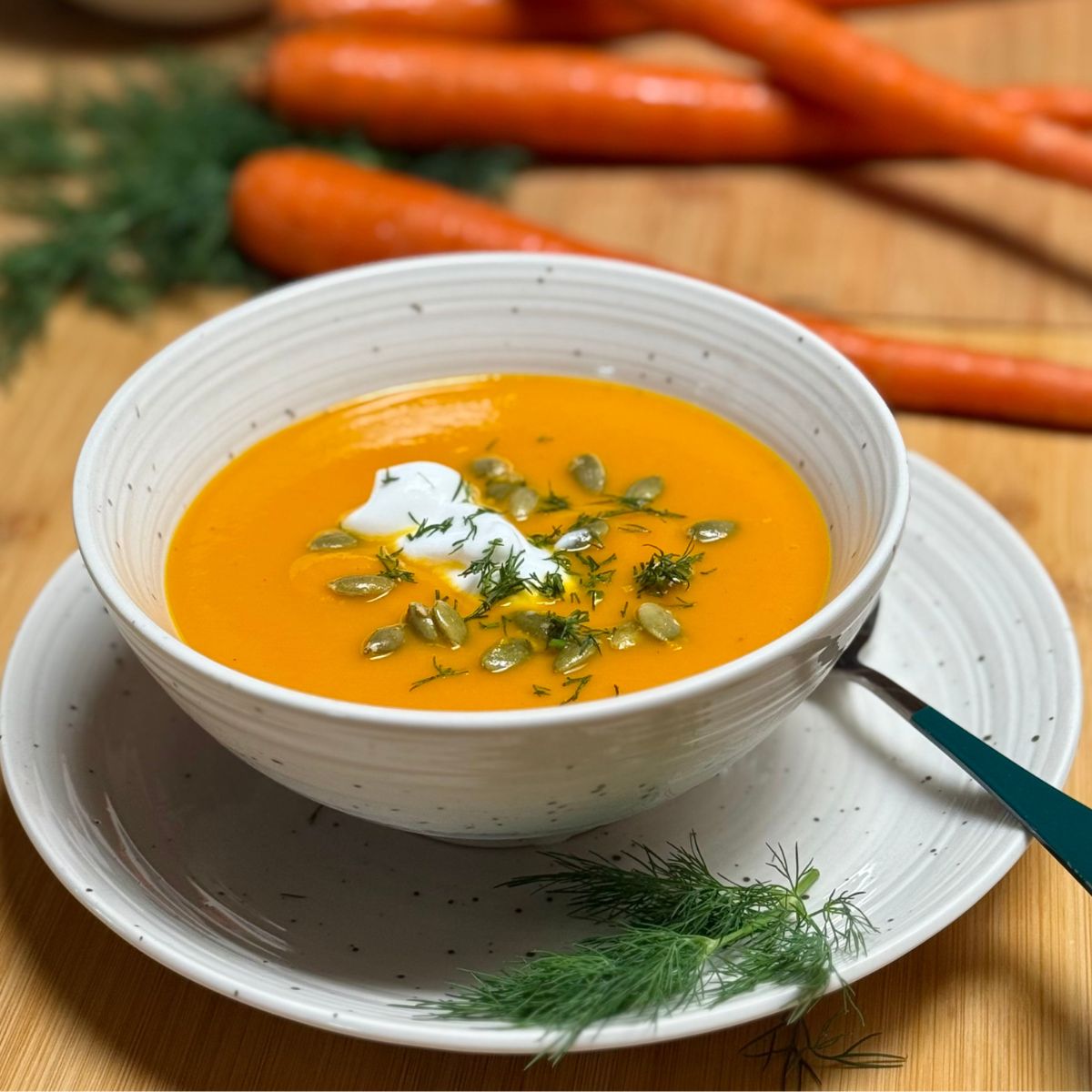 A bowl filled with vegan carrot ginger soup garnished with non-dairy plain yogurt, pumpkin seeds and dill.