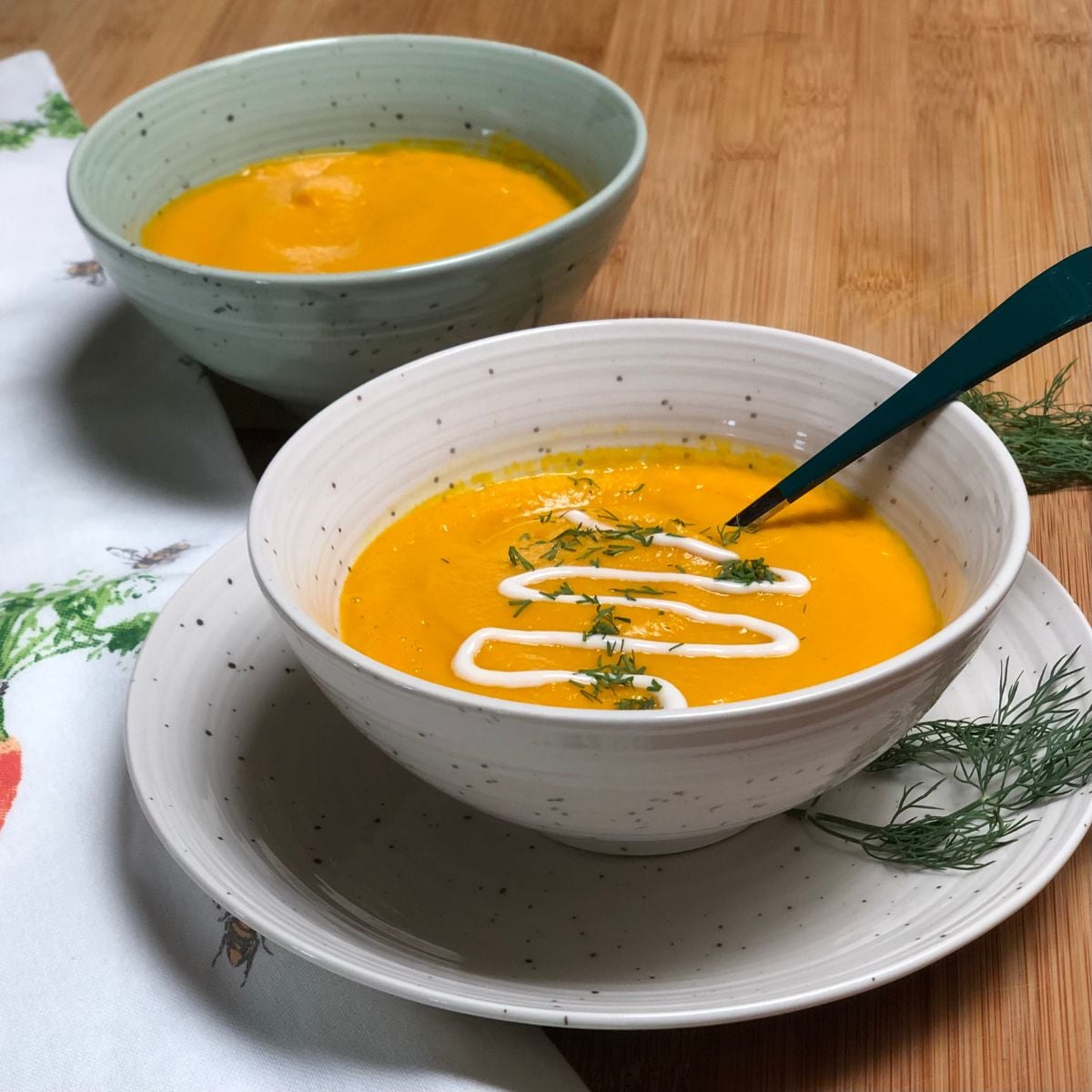 Two bowls filled with vegan carrot ginger soup and garnished with dill.