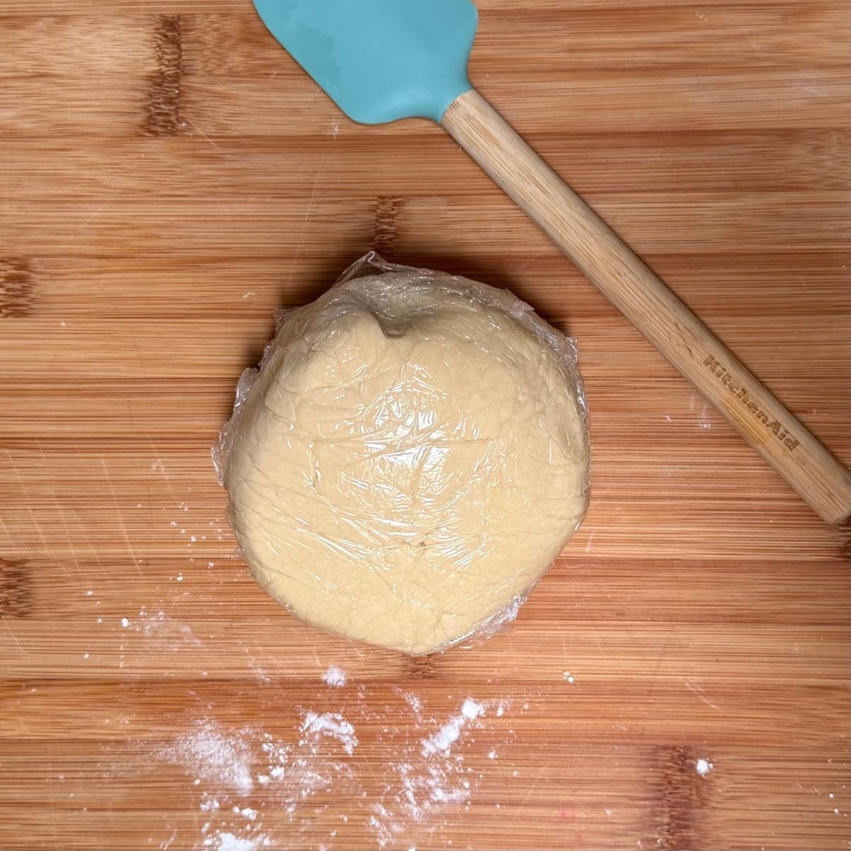 A ball of vegan shortbread cookie dough covered in plastic food wrap.