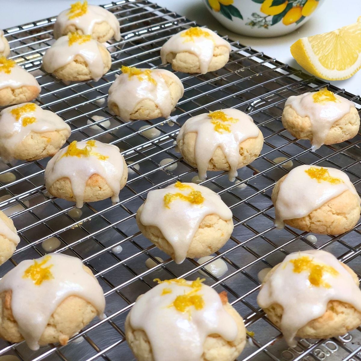 Vegan lemon drop cookies topped with lemon glaze icing and zest on a wire cooling rack.