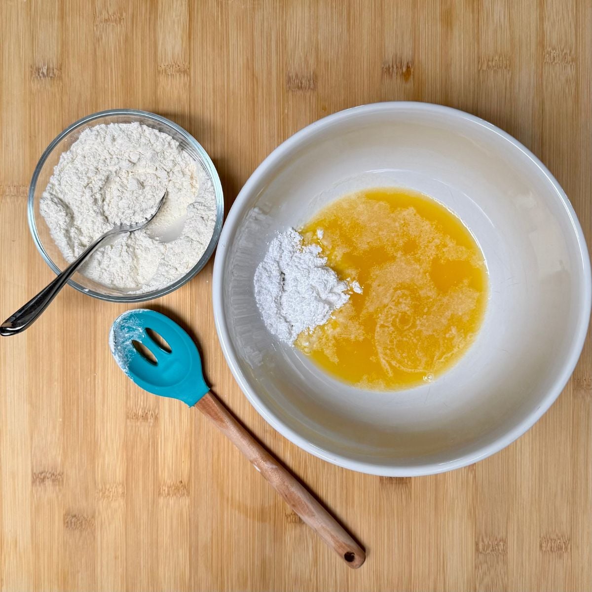 A mixing bowl with melted butter, powdered sugar and salt, next to a small bowl with flour.