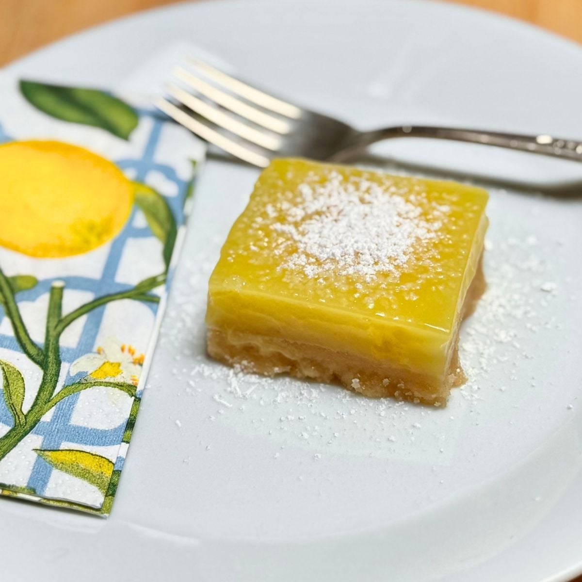 A square vegan lemon bar dusted with powdered sugar on a plate.