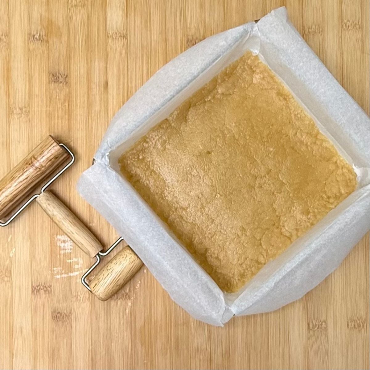 A square parchment lined baking dish with shortbread dough pressed in the bottom.