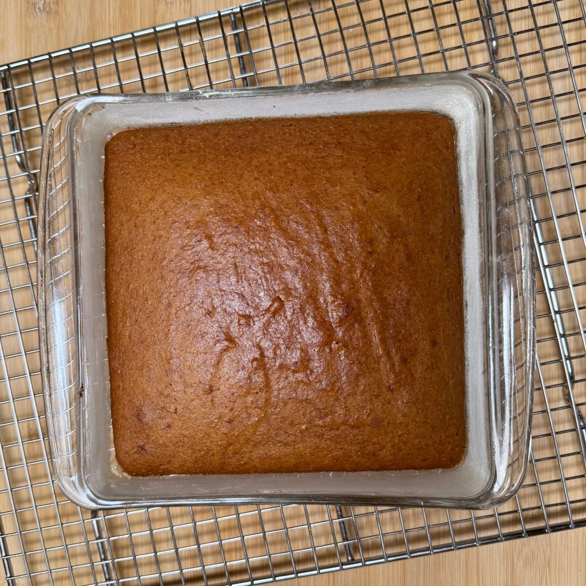 A vegan applesauce cake in a square baking dish on a cooling rack.