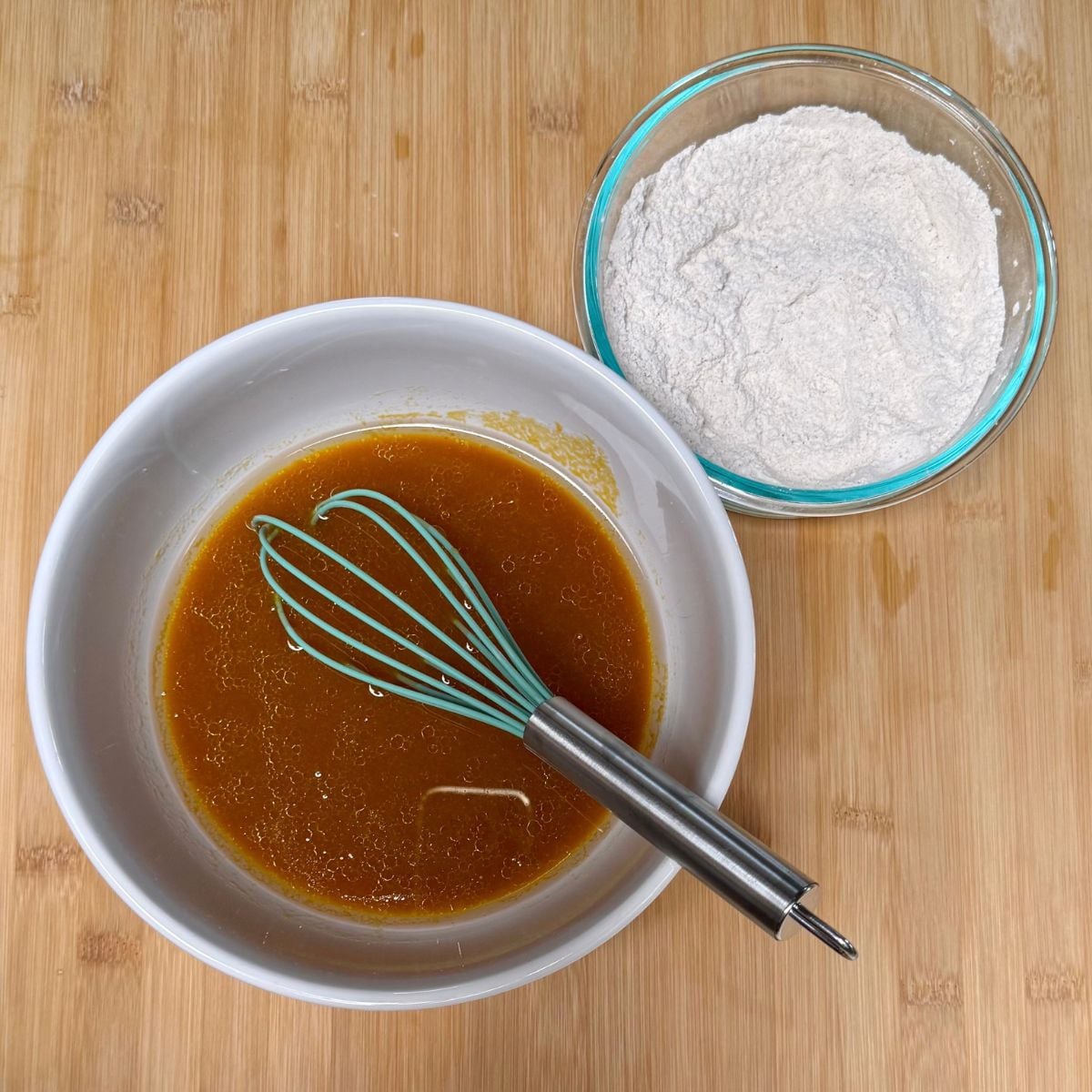 A bowl filled with combined wet ingredients for vegan maple pumpkin muffins and a bowl filled with the dry ingredients.