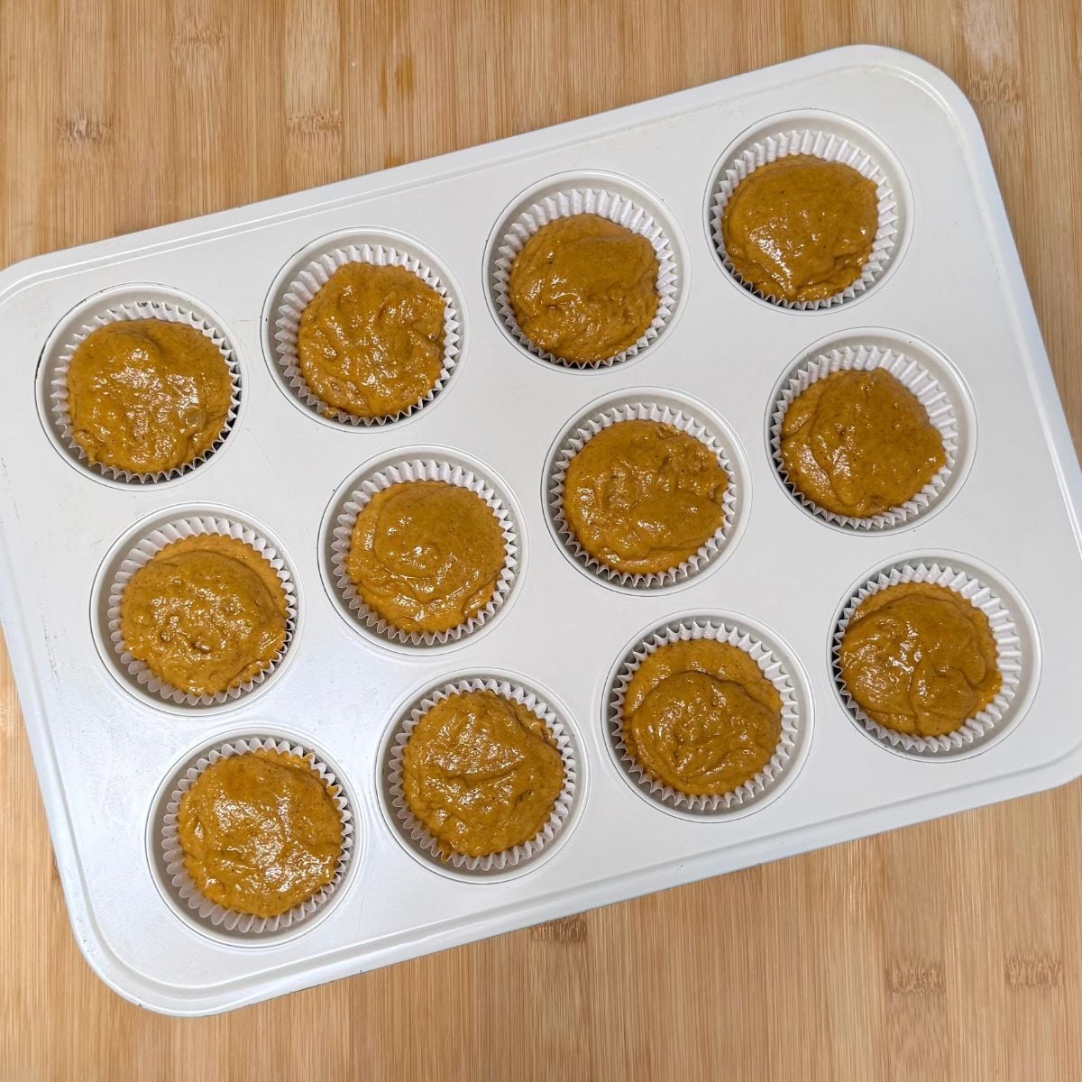 A muffin pan filled with pre-baked batter for vegan maple pumpkin muffins.