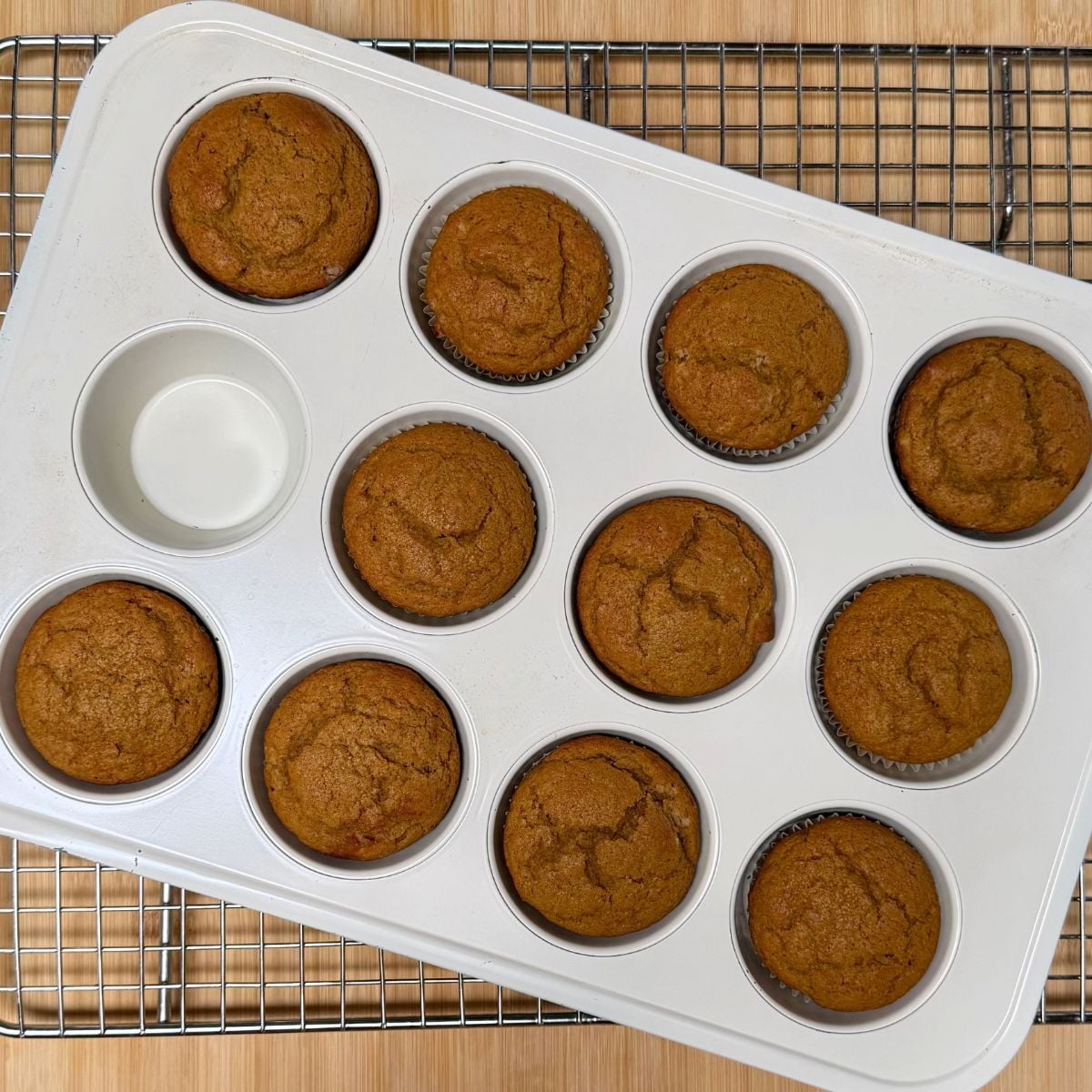 A muffin pan with 11 baked vegan maple pumpkin muffins.