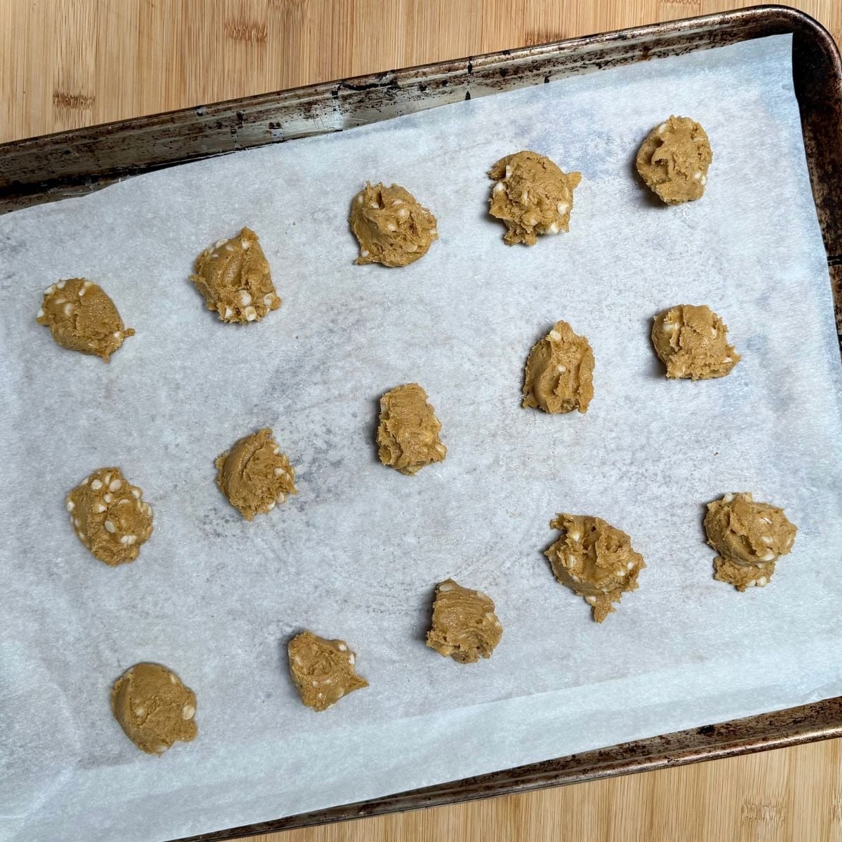 A parchment lined baking sheet with unbaked vegan pumpkin cookies with white chocolate chips.