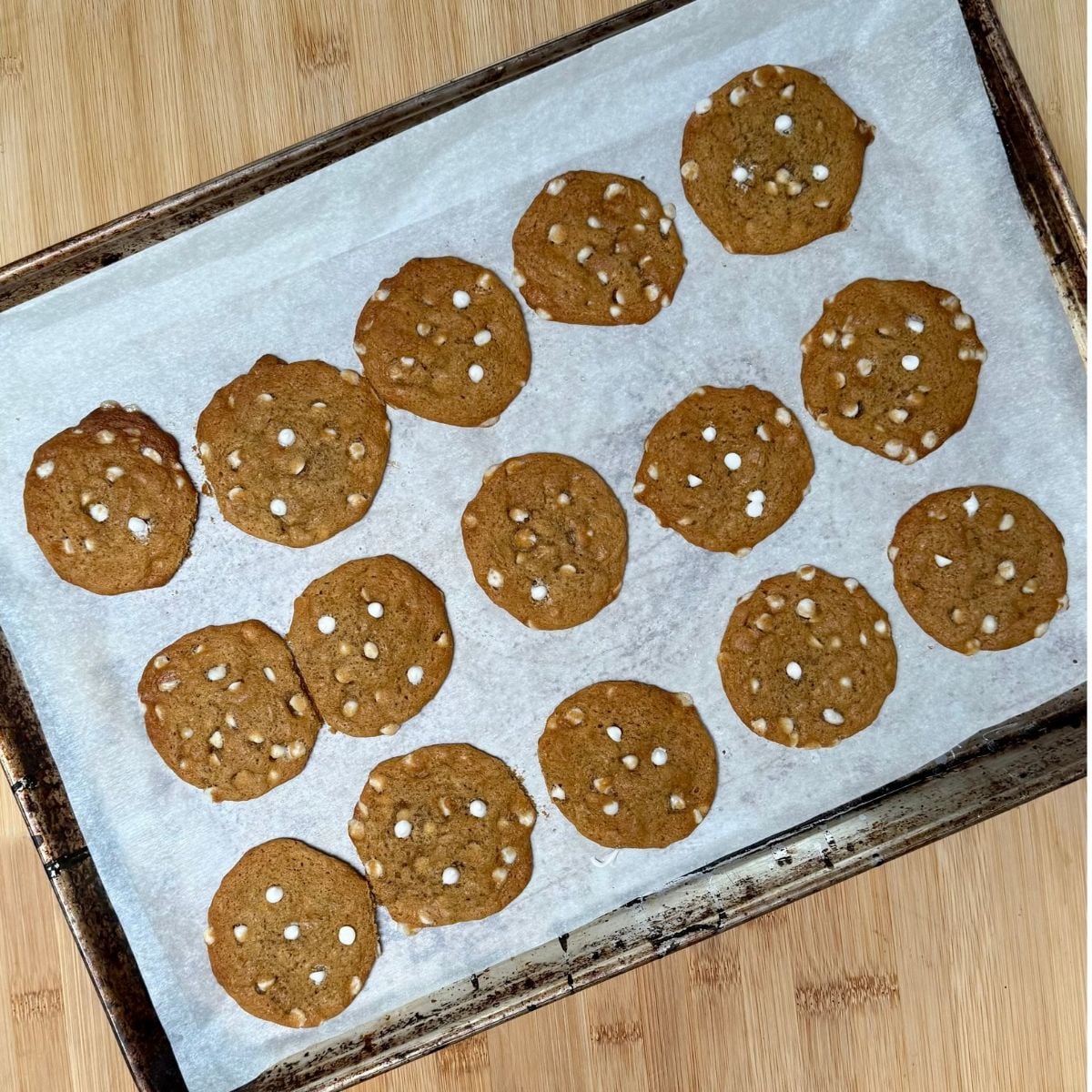 A parchment lined baking sheet topped with fresh baked vegan pumpkin cookies with white chocolate chips.