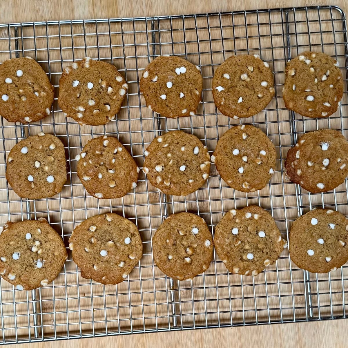 A wire cooling rack topped with baked vegan pumpkin cookies with white chocolate chips.